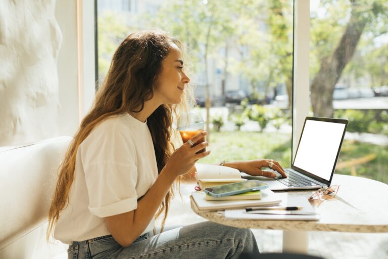 Young woman freelancer working in a coffeehouse, using her laptop and smartphone.
